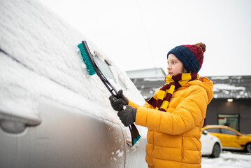 the boy helps his parents remove snow from the windshield of the car. Clear car window in winter from snow in winter.