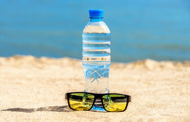 A bottle of drinking water and sunglasses on the sea beach