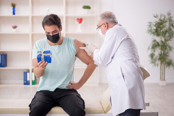 Old male doctor giving giftbox to young male patient