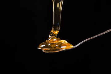 honey pouring into spoon isolated on black background