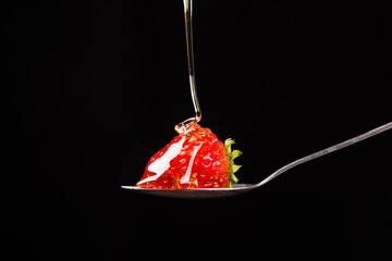 fresh strawberry on a spoon dipped in honey on black background