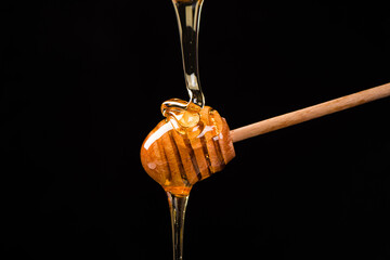 Wooden dipper with honey falling down isolated on black background