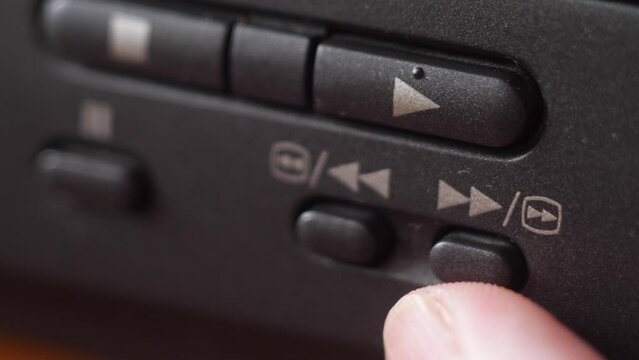 extreme closeup finger presses the play and fast forward button on the panel of the video recorder. Watching and fast forwarding a movie on your home device