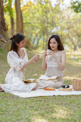 Two pretty asian friends woman picnic at park outdoor in relax time holiday, holiday recreation concept.