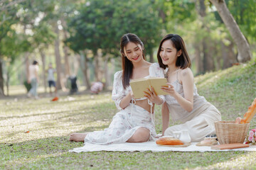 Two pretty asian friends woman picnic at park outdoor in relax time holiday, holiday recreation concept.