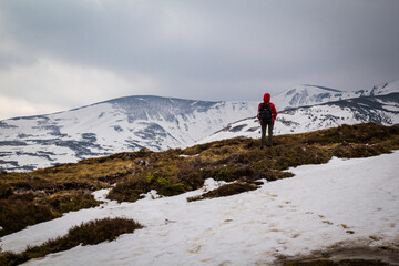 Fototapeta premium Hiker traveling across snowy mountain slopes landscape photo. Nature scenery photography with gloomy background. Ambient light. High quality picture for wallpaper, travel blog, magazine, article