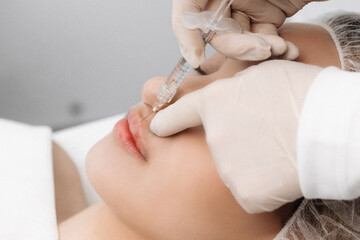 close-up, female lips. Surgeon, in medical gloves, carefully and slowly injects hyaluronic acid into woman's lips with a syringe. lip augmentation procedure. beauty injections. Plastic surgery.