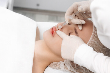 close-up, female lips. Surgeon, in medical gloves, carefully and slowly injects hyaluronic acid into woman's lips with a syringe. lip augmentation procedure. beauty injections. Plastic surgery.