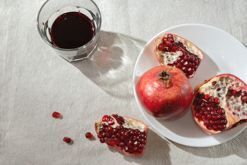 Ripe pomegranates on plate and wine in a glass on beige tablecloth with sunlight shadows, copy space