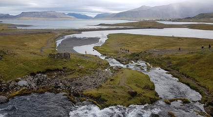 Tourists at Kirkjufellsfoss waterfall in Iceland with mountains at the background