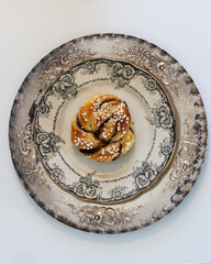  a homemade cinnamon bun on an antique plate that stands on a silver plate
