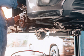 Technician man fixes a car's wheel hub and wheel bearing. replacement of the car's disk brake pads manually by a mechanic With a flare light effect and copy space, a man is in a garage.