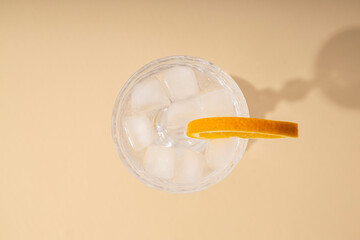 Glass with a cocktail with an orange slice on a beige background. Top view, flat lay