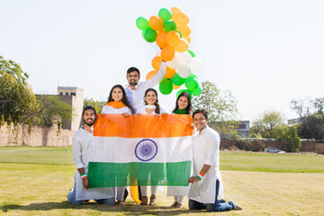 Group of happy young people wearing traditional white dress holding indian flag celebrating...