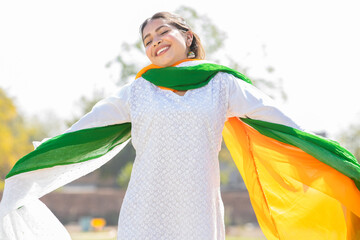 Portrait of happy young indian woman wearing traditional white kurta and tricolor duppata running at park. celebrating Independence day or Republic day.
