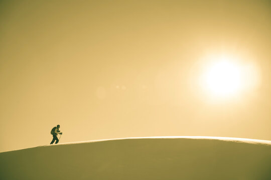 A skier crosses a snowy ridge in sunshine.