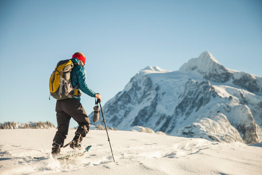 A female snowshoer crosses a snowfield with Mount Shuksan in the background.