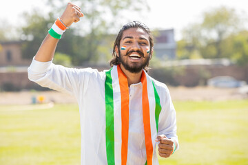 Portrait of cheerful young man fan wearing traditional white kurta and tricolor duppata with face...