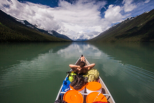 A young relaxes in the front of a canoe while canoeing across Lanezi Lake.