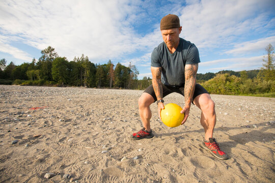 Fit Man Completes Squats With A Medicine Ball During An Outdoor Exercise Routine