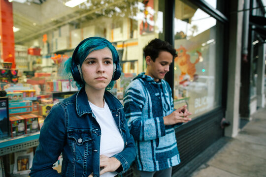 Teen girl wearing headphones standing outside of shop next to brother