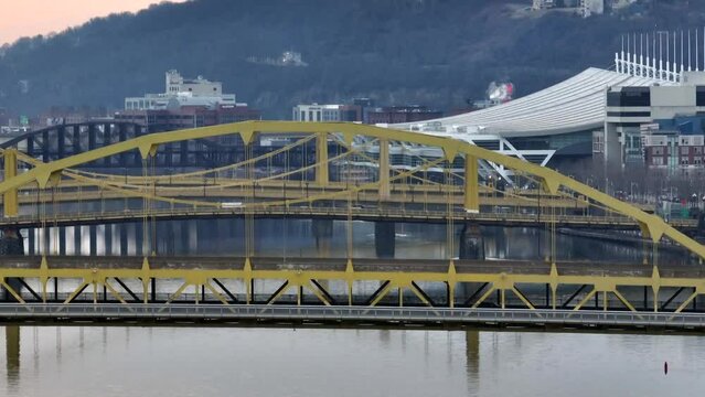 Aerial rising shot of yellow steel bridges in Pittsburgh PA. David Lawrence convention center in city in background. Long aerial zoom.