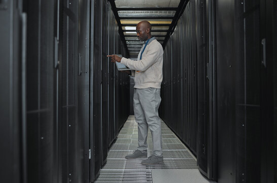 Laptop, maintenance and server room with IT black man for research, engineer working in dark data center. Computer, cybersecurity and analytics with male programmer problem solving or troubleshooting