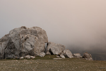 Big grey boulders on dim green slope with dense white cloud in mountains in dull frowning summer...
