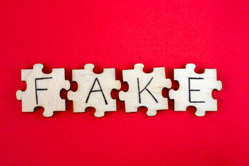 Learning FAKE. The hand lettering on the wooden puzzles is insulated on a white background. The word written on wooden puzzles lying on a red background