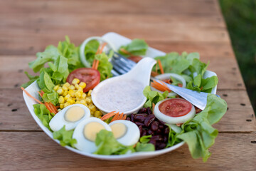 Bowl salad with vegetables and greens on wooden table.