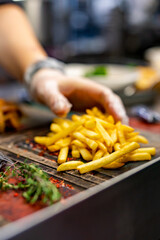 chef in cooking gloves serving french fries on wooden board.