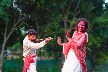 Fototapeta premium Indian man spraying color with water gun on woman at park. Holi festival concept.