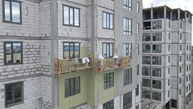 Industrial Climber Paints Wall of Building Facade with White Paint using Paintbrush. Slow Motion. Climbers on a suspended elevator paint the building. Thermal insulation. High quality 4k footage