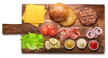 Cheeseburger ingredients on wooden board. File contains clipping path. Flat lay.