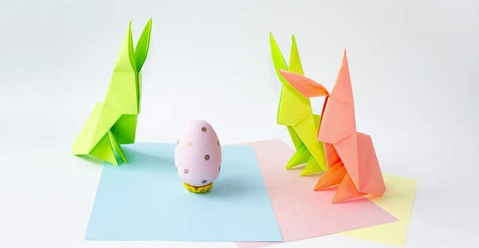 Craft, oregami Easter bunnies from colored paper on a white background and an Easter egg.  The concept of children's creativity, a bright Easter holiday.  Front view.