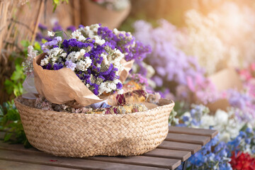 Beautiful small violet or purple flowers in a straw basket on a wooden table with other flowers on the background outdoors with sun rays