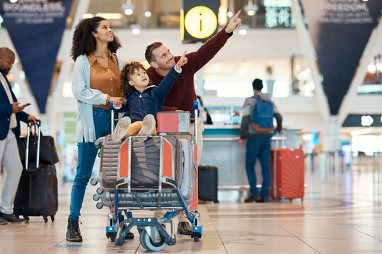 Pointing, Travel And Interracial Family At The Airport Looking At A Departure Time For A Flight. Happy, Trip And Parents With A Child To Look At Information For Arrival Or Leaving Of An Airplane