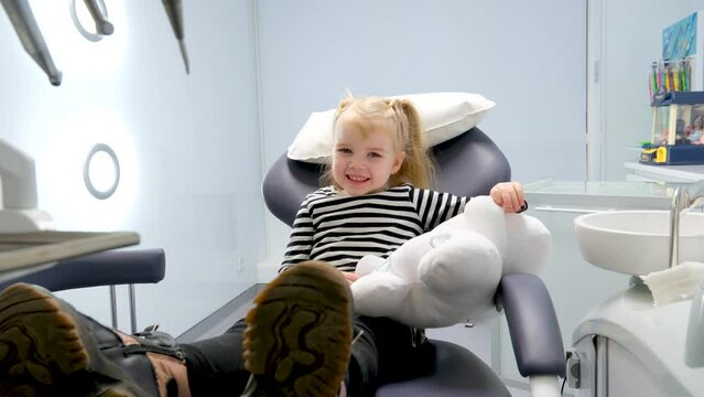 beautiful little blond blonde girl in dentist office big shoes on feet close-up latest technology soft toy in hands smile meeting the doctor alone in frame slow slow motion camera zooms in and out