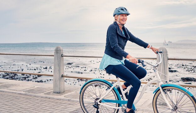 Happy, smile and cycling with old woman at beach for fitness, peace and travel with blue sky mockup. Relax, workout and retirement with senior lady riding on bike for nature, health and wellness
