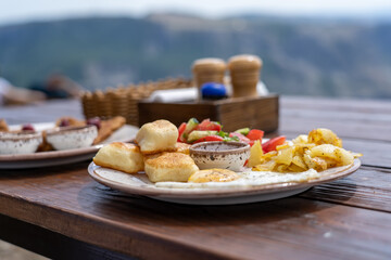 Breakfast with scrambled eggs, tomato salad on white ceramic plate on wooden table on mountain...