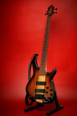 Full scales 5 strings bass guitar at stand with natural finish, isolated on red background