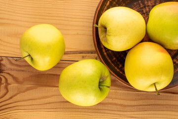 Several yellow organic apples with clay plate  on wooden table, macro, top view.