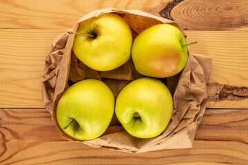 Four yellow organic apples in a paper bag on a wooden table, macro, top view.