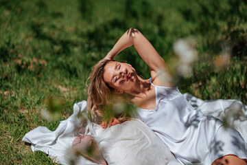 woman sleeps on a white bed in the fresh spring grass in the garden. Dressed in a blue nightgown.