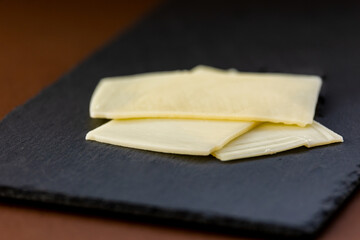 close up cheese on black stone board at brown background