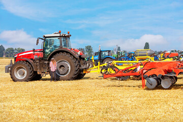 Obraz premium Agricultural machinery at the exhibition, powerful multi-row disc harrow with a tractor against the backdrop of an agricultural field.