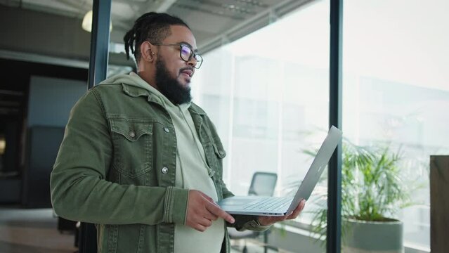 Business man holding a laptop and discussing with his team. Software developer having a meeting in an office. Young black man working in a tech company.