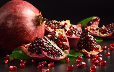 Clusters with ripe pomegranate arils on black background. Fresh pomegranate seeds. Cut open fruit...