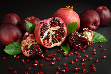 Split open fruit scattered red grains seed indoors. Still life ripe pomegranates, red apples, green...