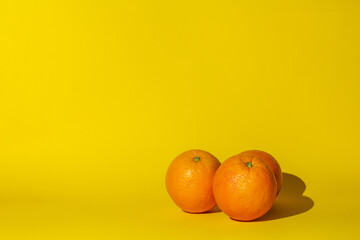 oranges fruits citrus ,three objects,hard shadow,orange color round,lie on the surface of the yellow background.concept juice vitamins.